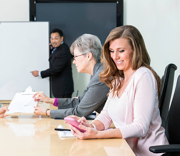 mulher olha para o seu telemóvel durante a reunião de negócios - inconvenience meeting business distracted imagens e fotografias de stock