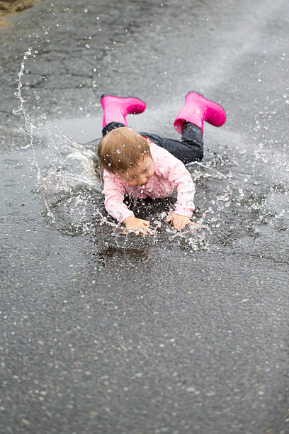 istock Little Girl Falling Into a Puddle of Rain 477435312