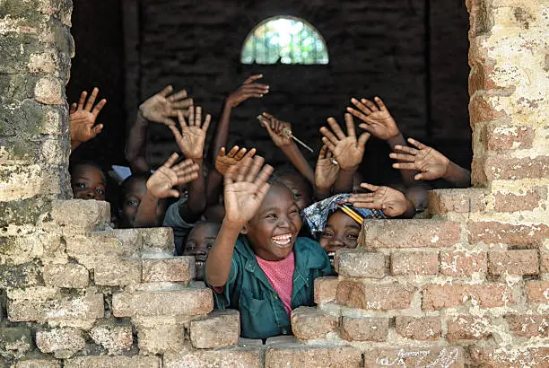 A group of african children inside of a destroyed school, wave hands and say hello.