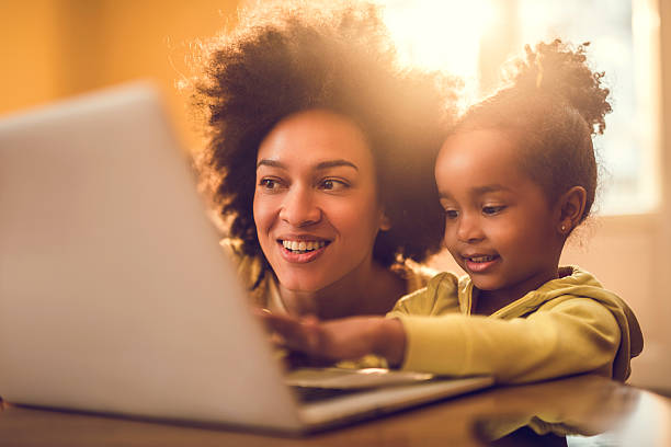 jovem afro-americana mãe e sua pequena menina usando computador. - child computer laptop little girls imagens e fotografias de stock