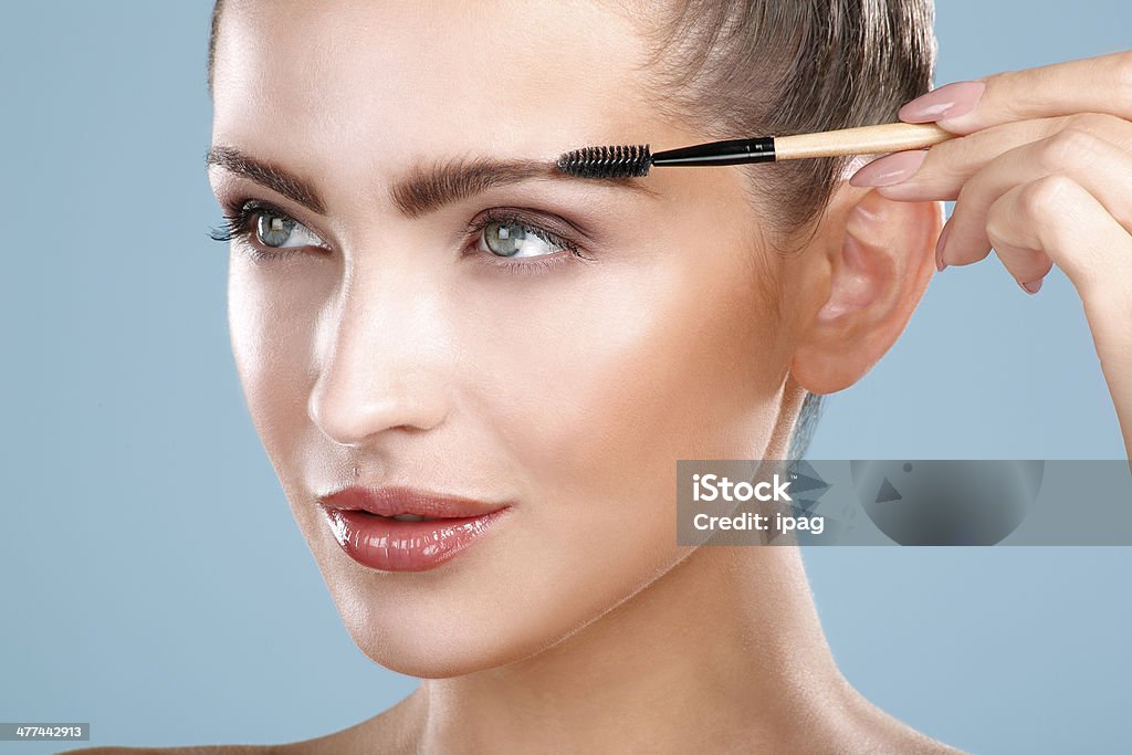 Closeup beautiful woman with eyebrow brush tool Closeup beautiful woman with eyebrow brush tool on blue Eyebrow Stock Photo