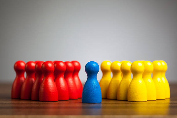 Single blue pawn figure between red and yellow groups stock photo
