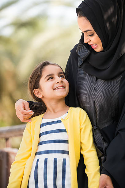 Traditionally Dressed Middle Eastern Mother Holding and Smiling with Daughter stock photo