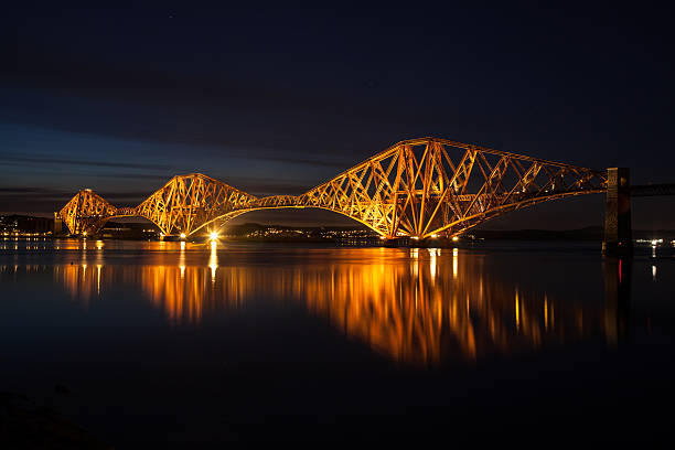 Forth Rail Bridge over the Firth of Forth in Scotland; Lights eliminate the bridge against the night sky. Lights are reflected on the water