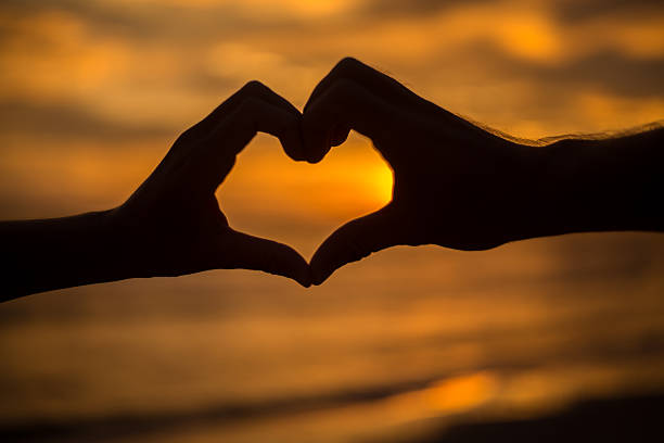 istock Silhouette of hands on beach at sunset making heart shape. 477450456