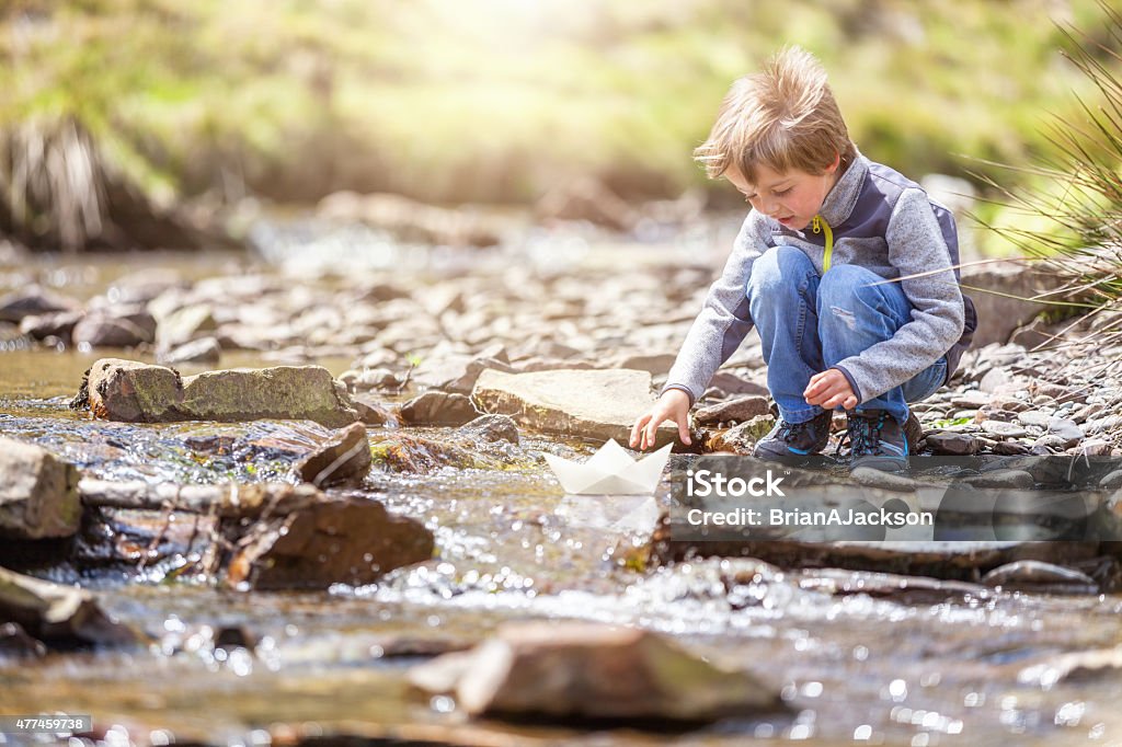 Boy sailing a paper boat Child playing in summer sunshine with a paper boat in stream Child Stock Photo