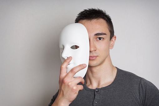 young man taking off plain white mask revealing face               