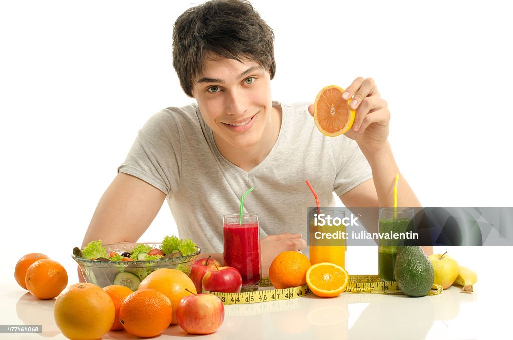 Man having a table full of fruit, juices and smoothie. Cheerful young man eating healthy organic food, salad and fruits, dieting. 2015 Stock Photo