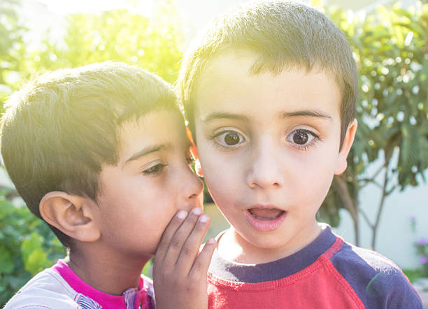 Little boy whispering something his friend's ear  There is sunlight effects in imamge. Image taken in backyard and developed from Raw.