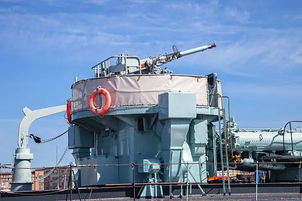 Gun turret on a naval warship over blue sky.