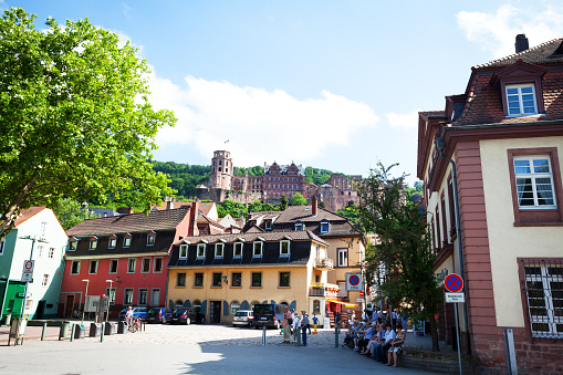 Heidelberg, Germany - June 3, 2015: Castle of Heidelberg seen from Neckarmünzgasse close to Neckarstaden. People and toruists are in street. At right side a group of tourists is sitting.