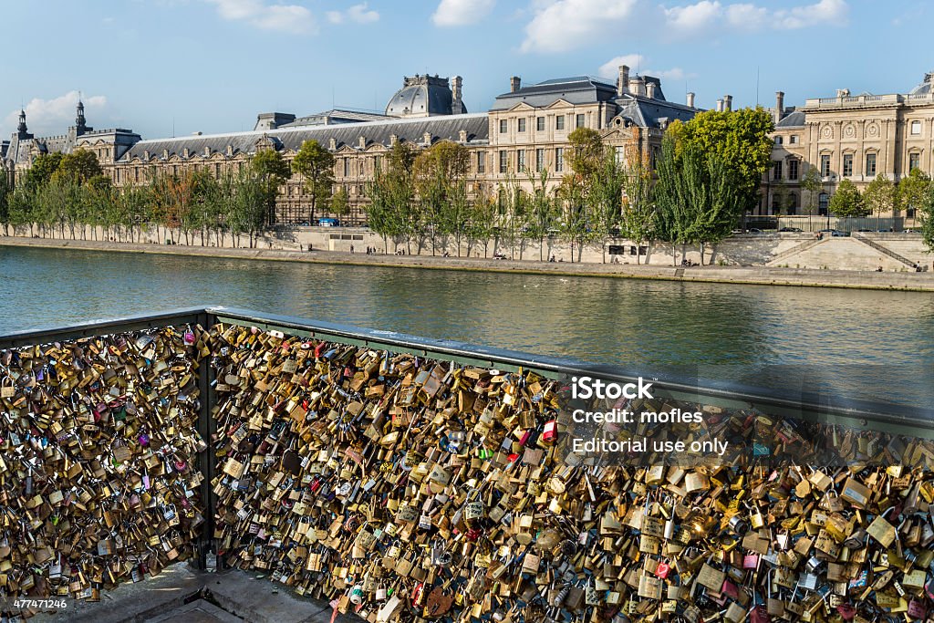 Love padlock frenzy with Louvre museum in the background Paris, France - October 02, 2014: Paris, France - October 02, 2014: Padlocks at Passarelle des Arts Bridge that symbolize the desire for an eternal love. Parisians estimate that over 16000 lockers have been left by couples in love on Passarelle des Arts. 2015 Stock Photo