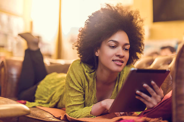 African American woman reading something from e-reader at home. Smiling African American woman enjoying at home and using digital tablet. e reader photos stock pictures, royalty-free photos & images