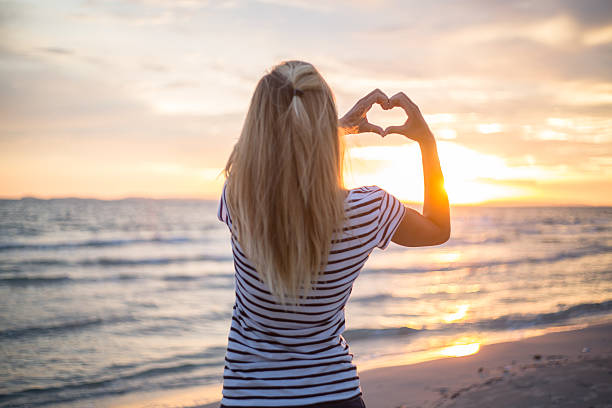 istock Girl on beach at sunset making heart shape with hands. 477475642