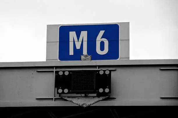 A Stylised black and white photograph, with the blue highlighted of an M6 motorway sign near Birmingham in England, UK.