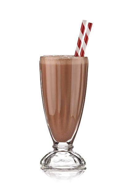 Classic glass of chocolate milkshake on white backdrop. Classic glass of chocolate milkshake with drinking straws standing on reflective white backdrop. There are two old-fashioned red-and-white straws standing in the glass. Visible reflection of the glass on the foreground.  DSRL studio photo taken with Canon EOS 5D Mk II and Canon EF 70-200mm f/2.8L IS II USM Telephoto Zoom Lens chocolate shake stock pictures, royalty-free photos & images