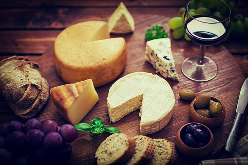 Glass of red wine surrounded by a variety of cheeses,olives and grapes