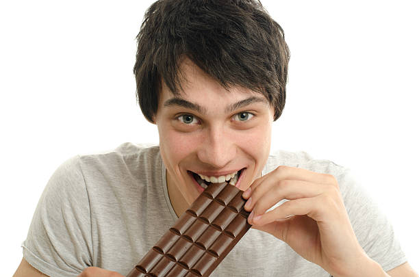 Happy man eating a yummy bar of chocolate. Happy man eating a yummy chocolate and having some sugar for an active day. Sweet cravings. man hand holding candy bar stock pictures, royalty-free photos & images