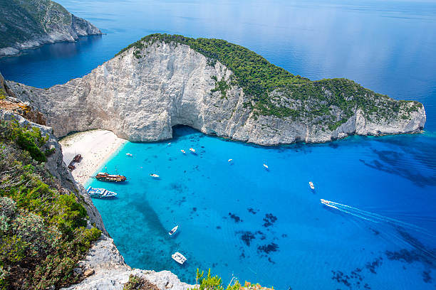famous Navagio Bay with shipwreck, Zakynthos island, Greece Tourists and tourist boats  in the famous Navagio Bay, Zakynthos island, Greece. The beach of Navagio with the old shipwreck is one of the main tourism spots of Zakynthos island in Greece - beside of the wreck its the turquoise sea what makes this place so famous. zakynthos stock pictures, royalty-free photos & images