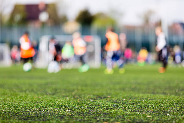 Blur of young boys playing soccer match Shallow depth of field shot of young boys playing a kids soccer match on green turf. junior level stock pictures, royalty-free photos & images