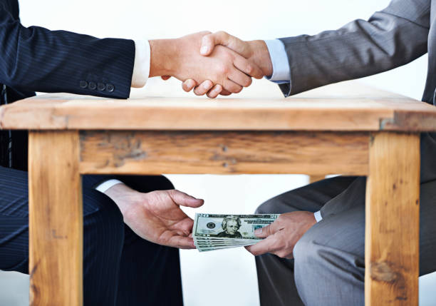 Under-the-table transactions... Cropped shot of two businessmen shaking hands while money passes hands under a table corruption stock pictures, royalty-free photos & images