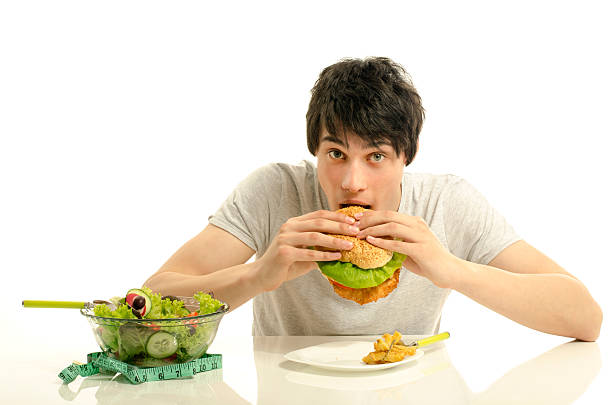 istock Young eating a big hamburger instead of the salad. 477517460