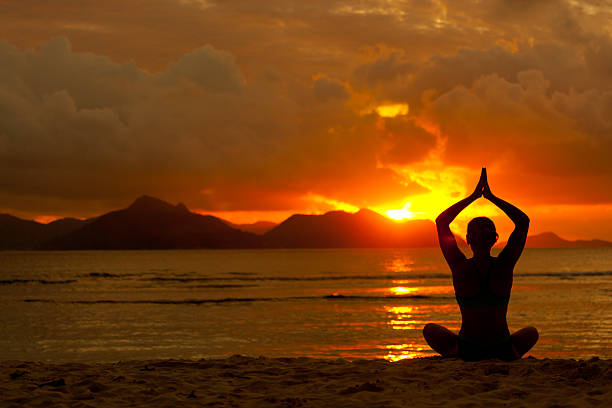 silhouette of woman sitting in yoga pose on beach at sunset 