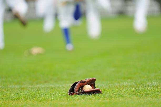 Baseball glove on ground Photograph of baseball in baseball glove on outfield grass as out of focus team stretches and warms up in the background.  Selective focus on foreground. fielding drills for baseball stock pictures, royalty-free photos & images