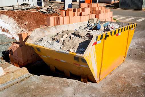 Photo of an yellow rubbish container at a construction site.