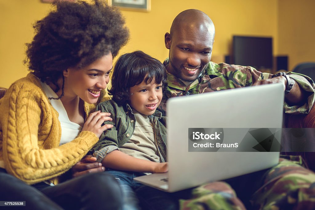 Happy African American military family using laptop at home. Happy military family relaxing at home and using computer together. African Ethnicity Stock Photo