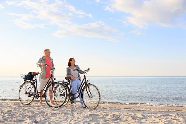 pareja madura al aire libre en la playa - action mature adult bicycle senior couple fotografías e imágenes de stock