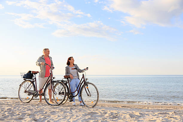 casal ao ar livre na praia - action mature adult bicycle senior couple imagens e fotografias de stock