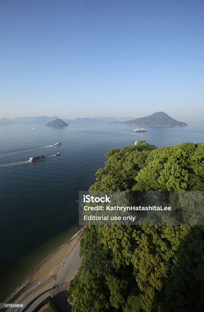 Spring Morning in Hiroshima Bay, Inland Sea, Japan Hiroshima, Japan - May 26, 2015: Spring Morning in Hiroshima Bay, Japan. Marine vessels ply their way between the islands in Hiroshima Bay. Foreground includes green foliage near the water's edge. Hiroshima City Stock Photo