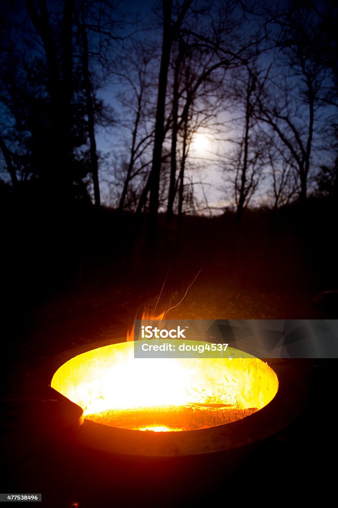 Roaring Campfire on a Moonlit Night A campfire burns in a round fire pit on a moonlit evening.  Shot in the woods of northern Michigan with a wide angle 20mm 1.8 lens and a high resolution Nikon D800, this image communicates the feel of a camp fire on a chilly evening. 2015 Stock Photo