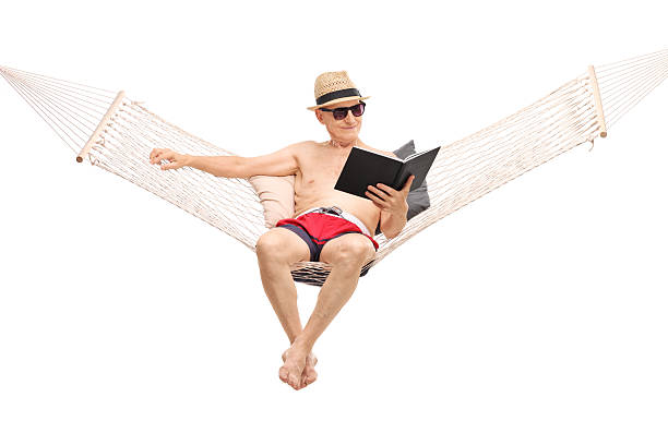 istock Relaxed senior sitting in a hammock and reading book 477543174