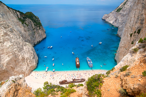 Tourists and tourist boats  in the famous Navagio Bay, Zakynthos island, Greece. The beach of Navagio with the old shipwreck is one of the main tourism spots of Zakynthos island in Greece - beside of the wreck its the turquoise sea what makes this place so famous.