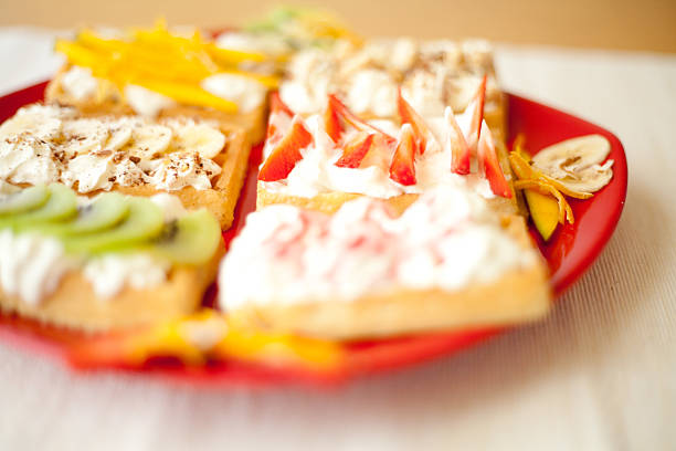 Sweet small waffles with whipped cream and different fruit fillings like strawberry, kiwi, banana, mango and chocolate topping. All prepared on red plate.