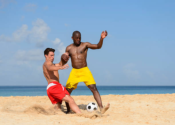 deux jeunes hommes jouant au football sur la plage - horizontal black and white toned image two people photos et images de collection