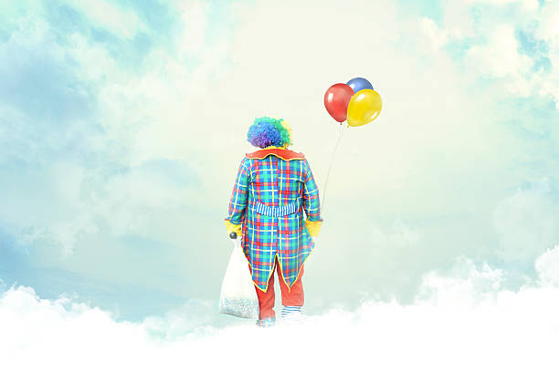 A male clown with happy joyful expression on his face posing behind a panel and holding balloons isolated on white background