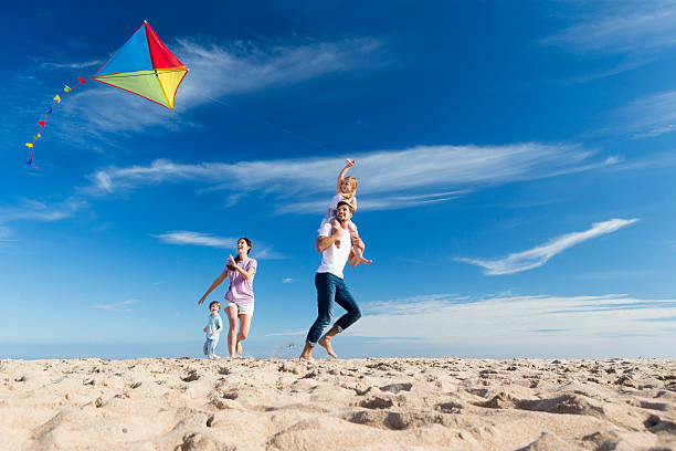 Family on the Beach Flting a Kite Family of four flying a kite on the beach beach play stock pictures, royalty-free photos & images