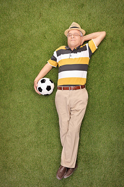 istock Mature man lying on grass and holding a soccer ball 477549126