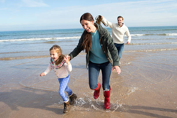 Family on the Beach Mother and daughter running away from dad who is chasing them with seaweed. couple tease stock pictures, royalty-free photos & images