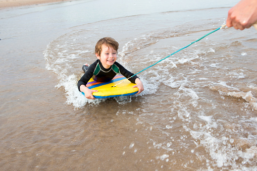Boy being pulled along the coast on a body board.