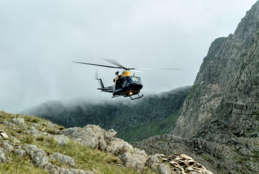 Mountain rescue helicopter flying into a mountain range covered in mist