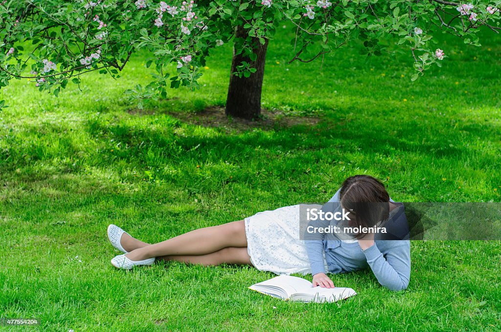 Young woman reads a book under blooming tree Young woman reads a book under blooming apple tree 2015 Stock Photo