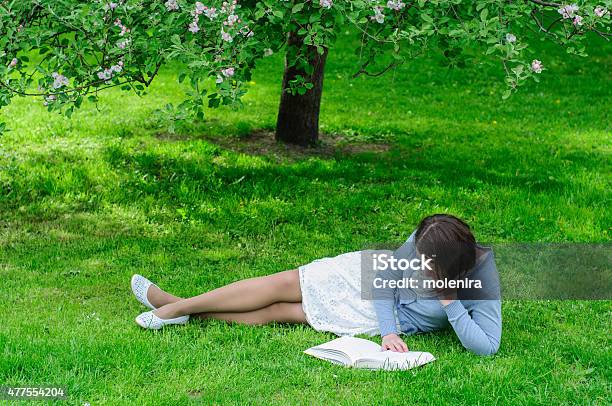 Young Woman Reads A Book Under Blooming Tree Stock Photo - Download Image Now - 2015, Adult, Apple - Fruit