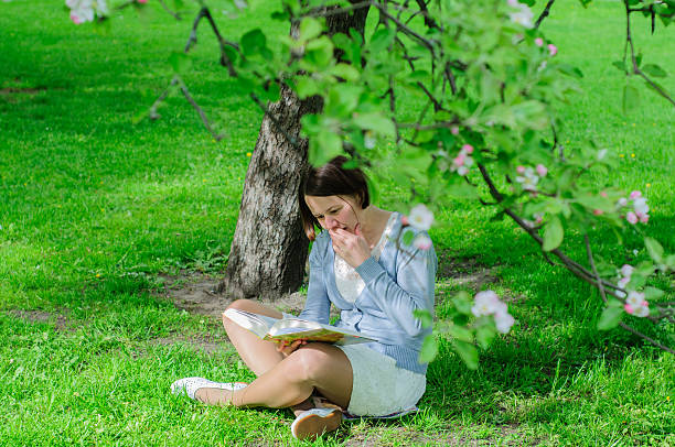 istock Young woman reads a book under blooming tree 477555236