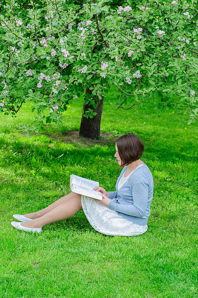 istock Young woman reads a book under blooming tree 477560574
