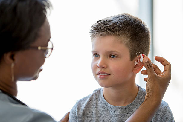 Medical Ear Exam A little boy is sitting on an examining table in a doctors office smiling at the nurse as she places a hearing aid in the child's ear. hearing loss photos stock pictures, royalty-free photos & images