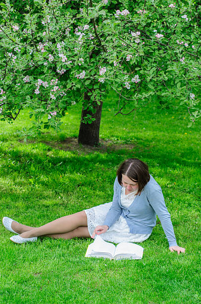 istock Young woman reads a book under blooming tree 477563280